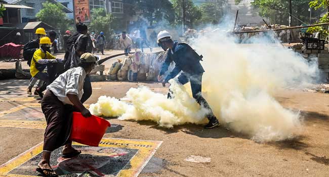 A man stands on a poster featuring armed forces chief Senior General Min Aung Hlaing as he attempts to douse tear gas during a crackdown by security forces on a demonstration by protesters against the military coup in Yangon’s Thaketa township on March 19, 2021. AF